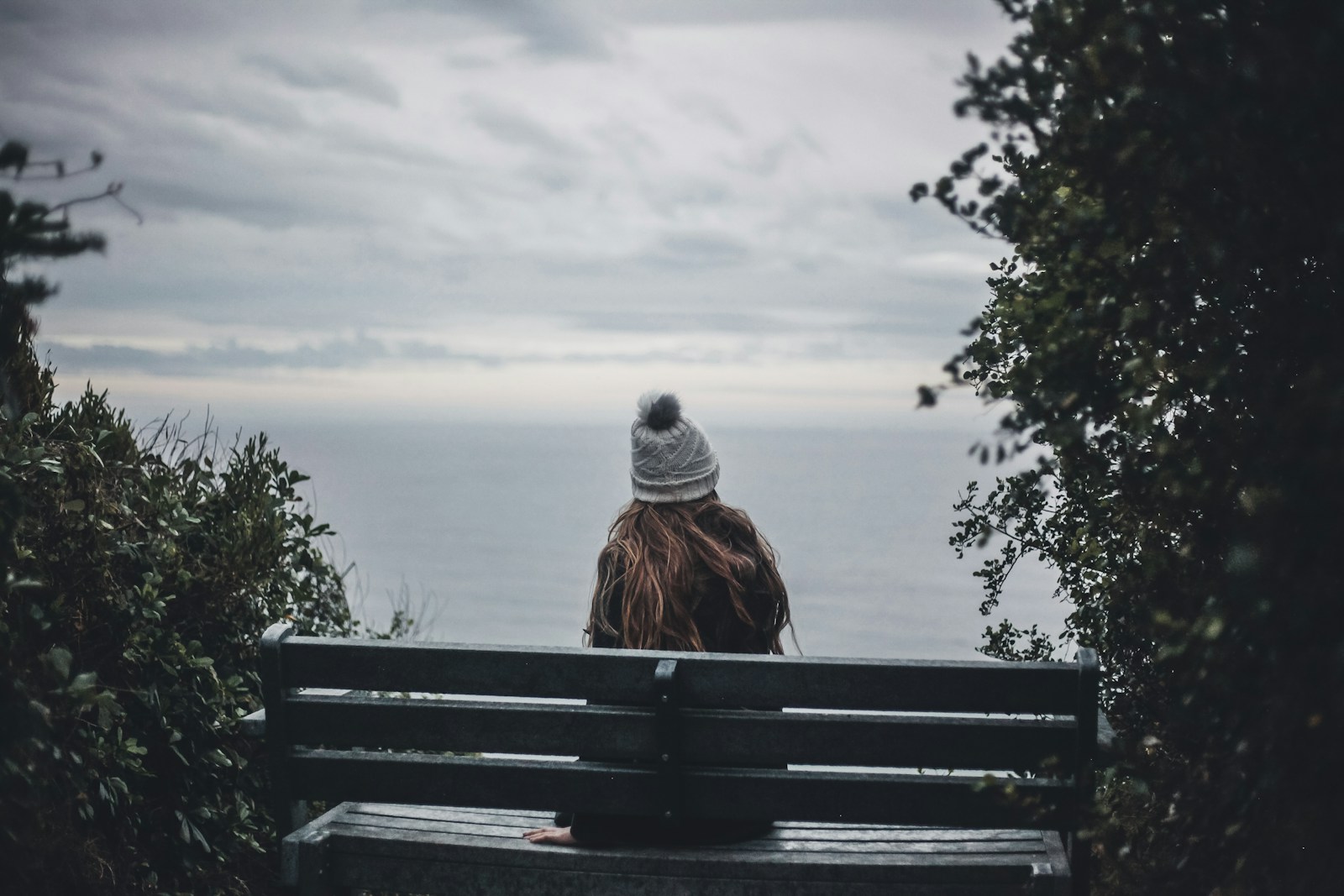 woman in gray knit cap sitting on brown wooden bench